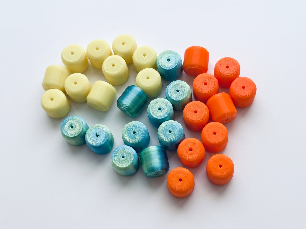 Cylindrical fishing rig floats with central holes, pictured in pale yellow, teal, and orange.
